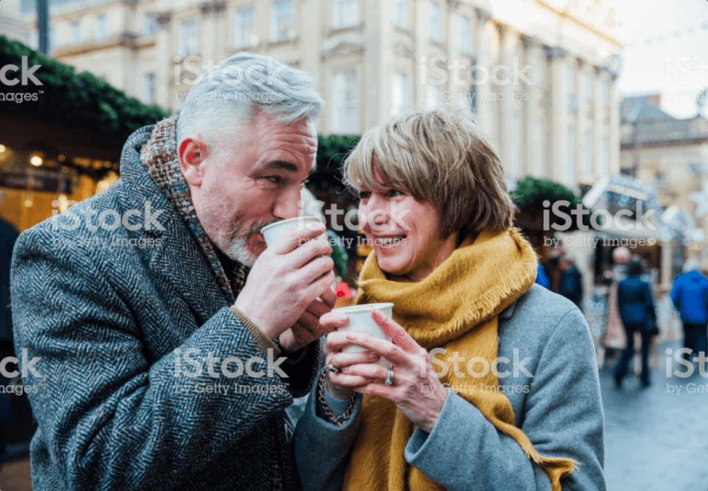 An older couple sipping a warm drink and smiling at one another.
