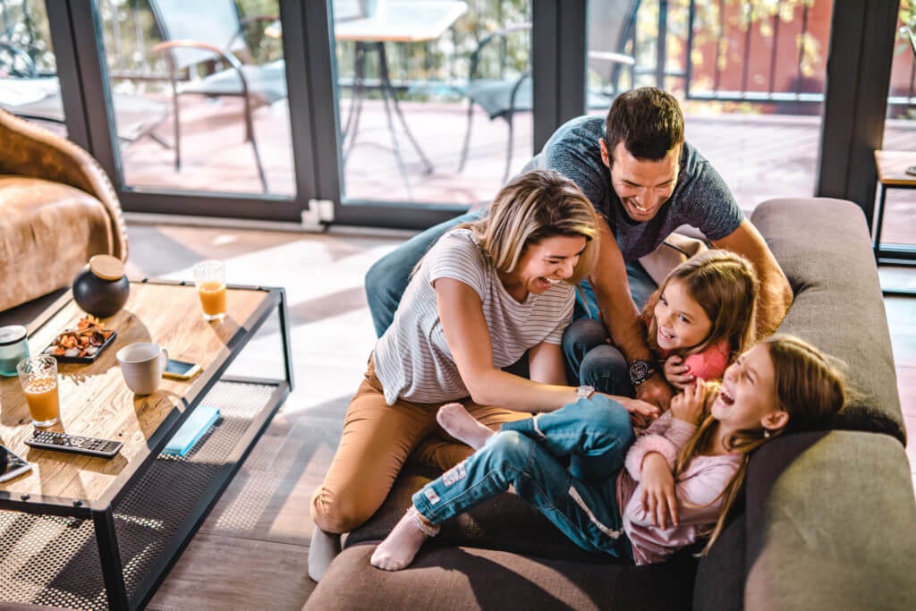 High angle view of cheerful parents having fun while tickling their daughters on sofa in the living room