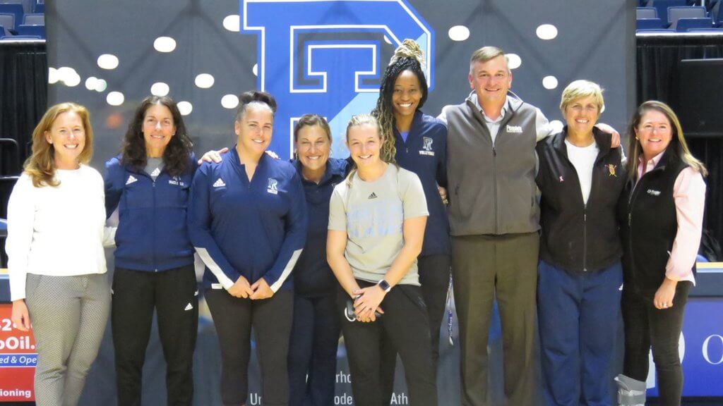 URI women's coaches with staff from People's Credit Union in front of URI sign